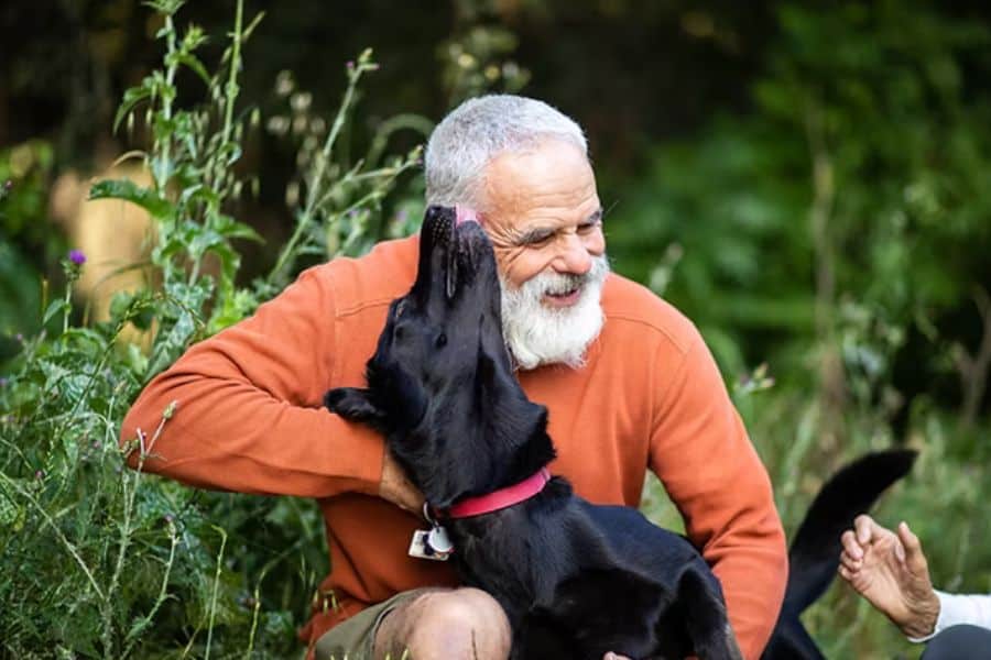 Elderly man with a black dog in a garden setting.