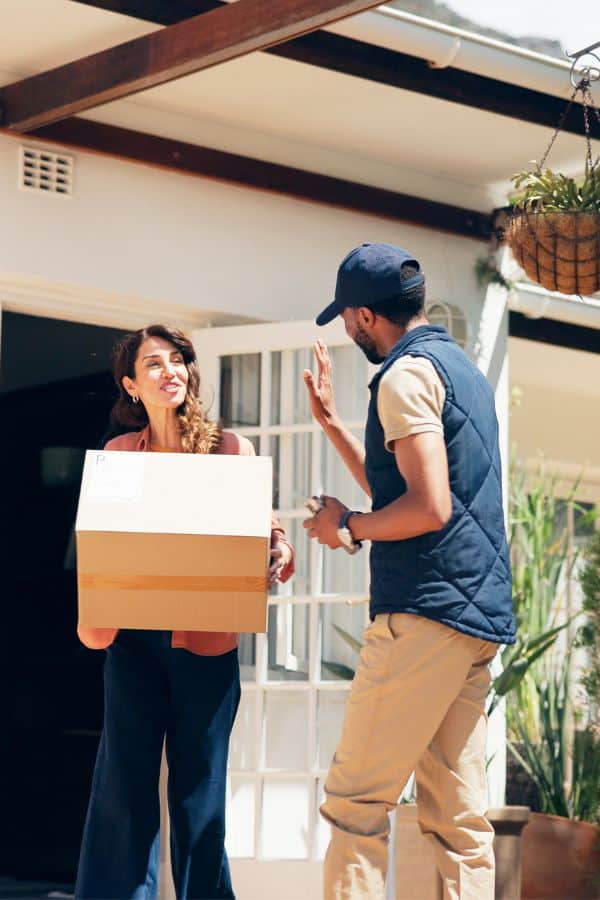 Delivery person handing package to woman at house entrance.